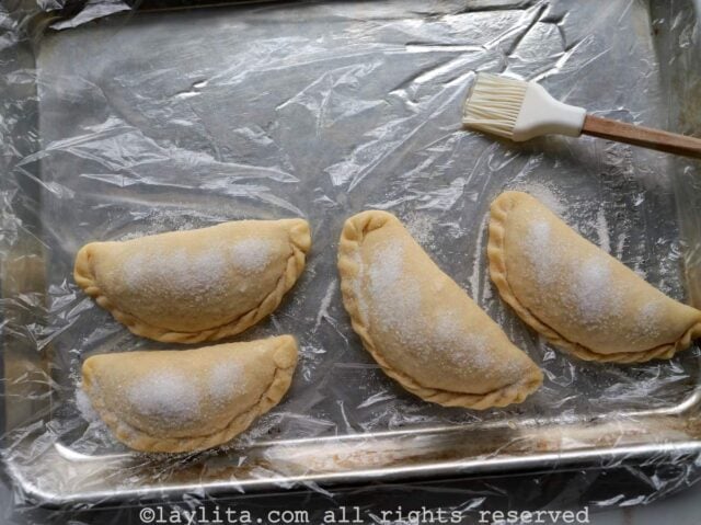 Empanadas brushed with oil and sprinkled with sugar on a pan