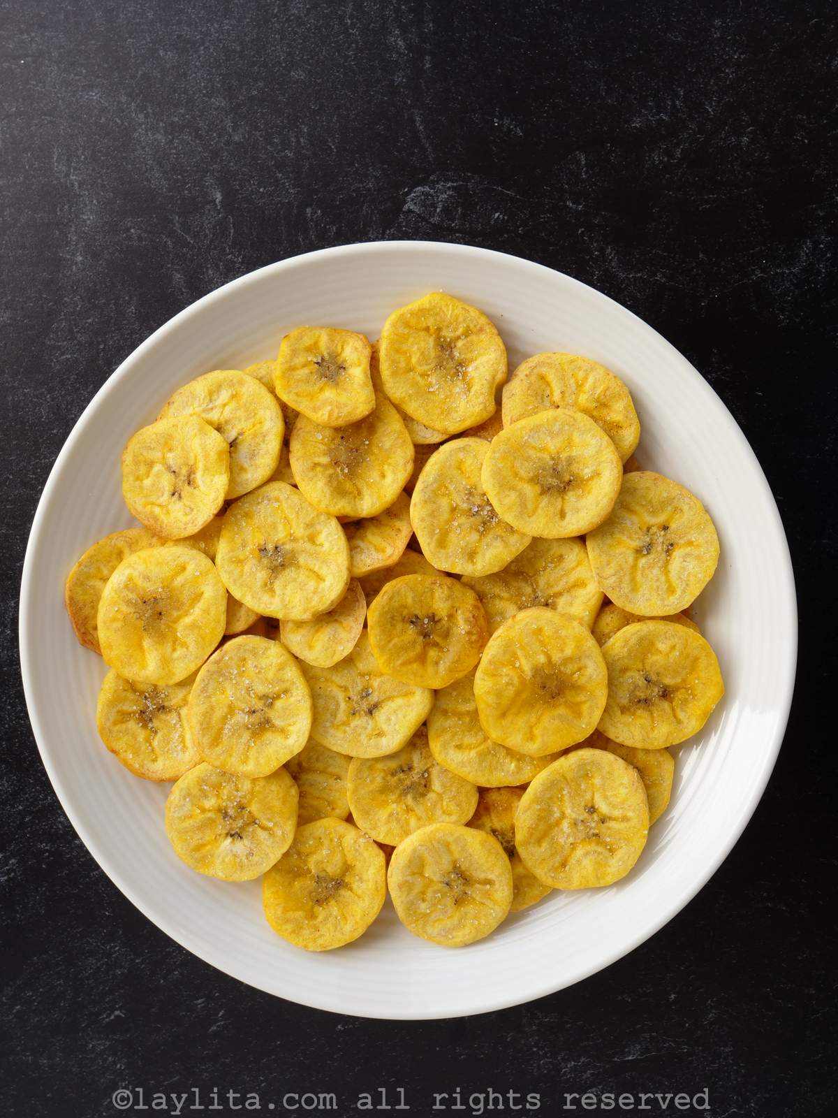 Overhead shot of air fryer plantain chips or chifles on a white plate with a black background