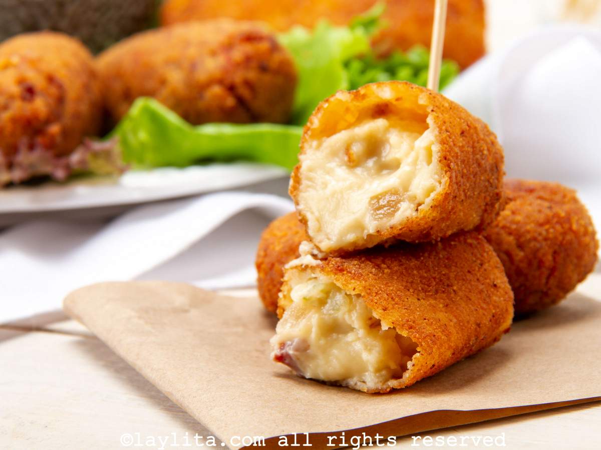 Two ham croquettes on a napkin with one broken in half to show the gooey inside.