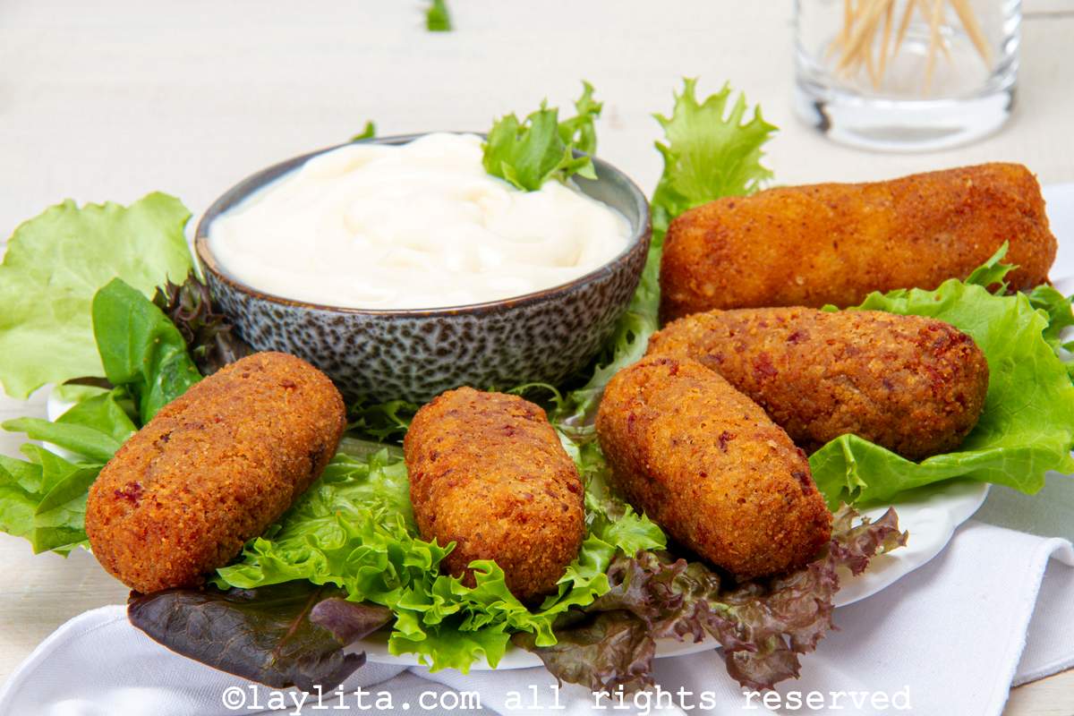 Side view of five Spanish ham croquettes served on a plate lined with lettuce and a dipping sauce on the side.