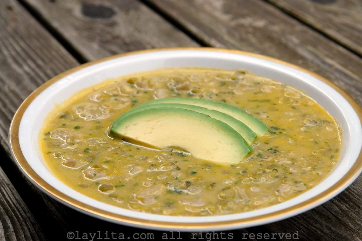 Arvejas con guineo or peas with green banana soup Soup of green banana and split peas in a white bowl with a golden rim on a wooden table, the soup is topped with avocado slices