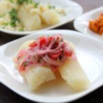 Boiled yuca topped with tomato onion salsa on a white plate