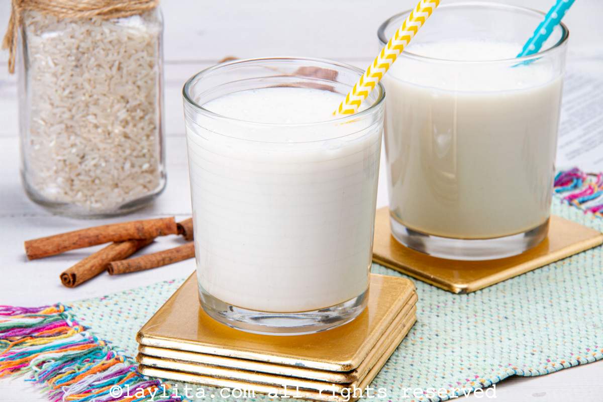 Two glasses of rice chicha on gold coasters with rice and cinnamon in the background.