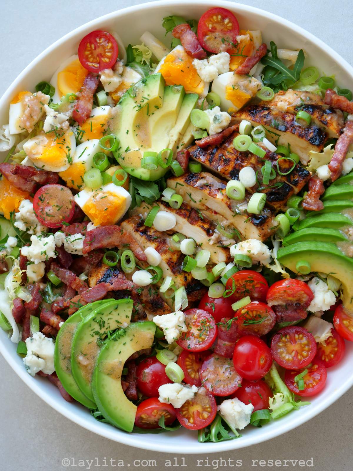 Overhead shot of a large bowl full of chicken cobb salad with sliced avocado, cherry tomatoes, boiled eggs, lardons and green onions