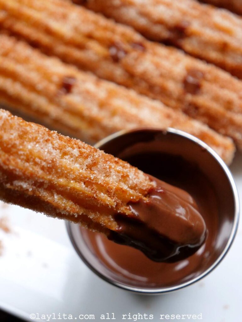 Close up of a churro being dipped in a small ramekin of chocolate sauce