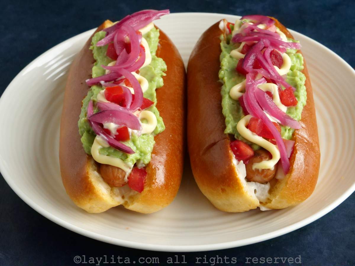 Side view of two Chilean hot dogs on a plate topped with pickled onions.