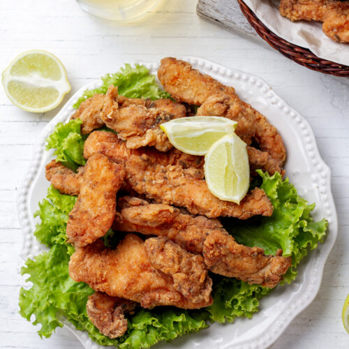 Chicharron de pollo on a white plate with two lime wedges on top