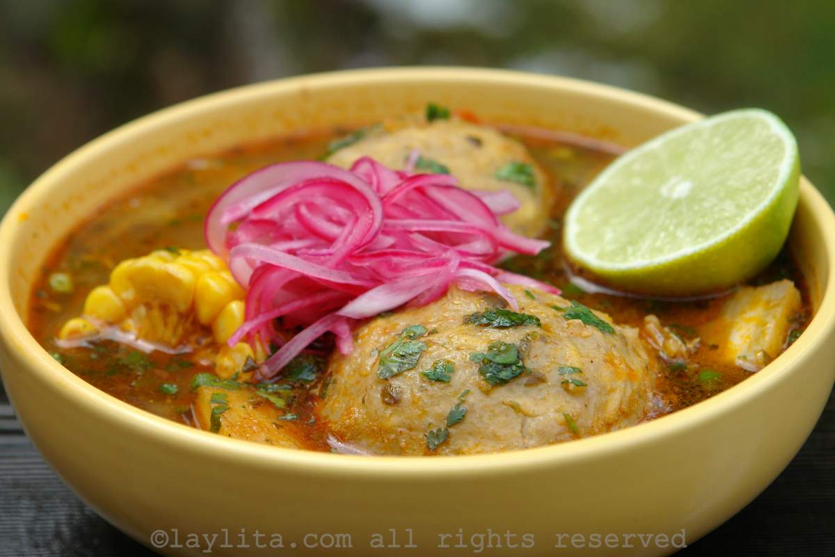 Caldo de bolas de verde or green plantain dumpling soup Ecuadorian caldo de bolas or green plantain ball soup in a yellow bowl, topped with pickled red onions and lime half
