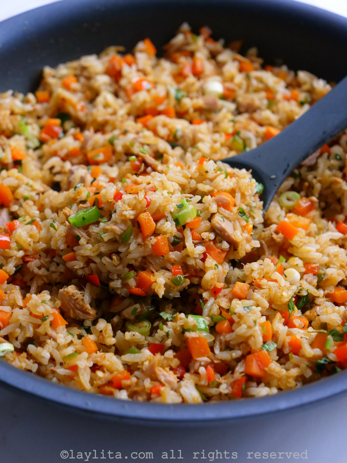 Tuna fish fried rice in a skillet with a rubber spoon lifting up a portion.