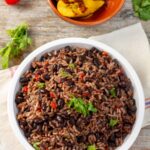 Overhead shot of gallo pinto in a white bowl served with a side of fried sweet plantains.