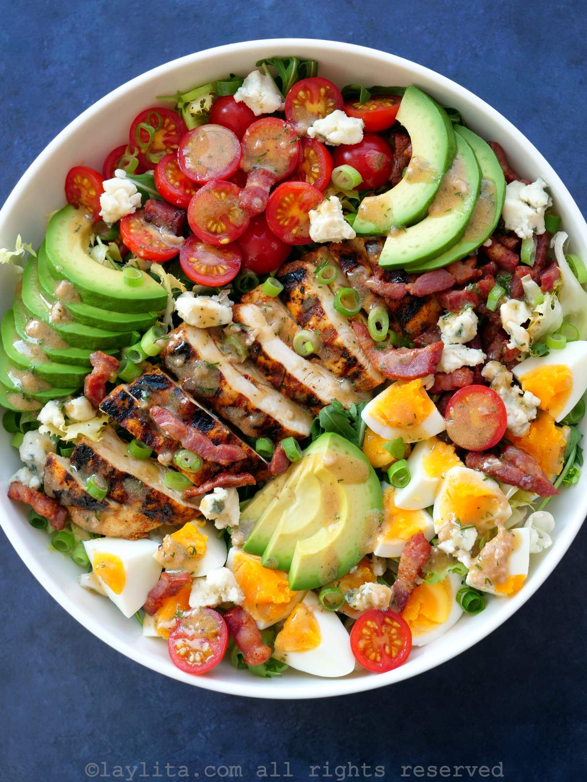 Chicken cobb salad served in a white bowl on a blue background