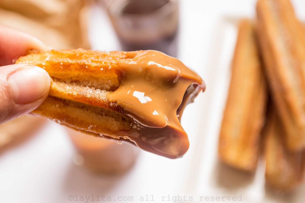 Hand holding a churro with a bite off it and the end dipped in caramel or dulce de leche