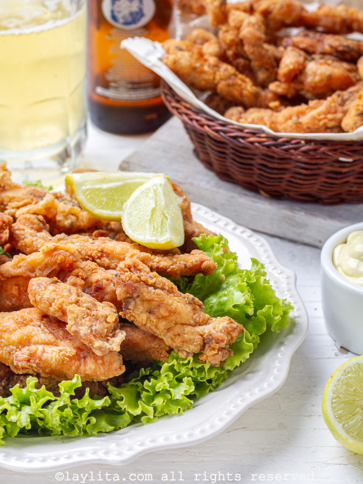 Side view of chicharrones de pollo served on a bed of lettuce on a late with more chicken in the background.