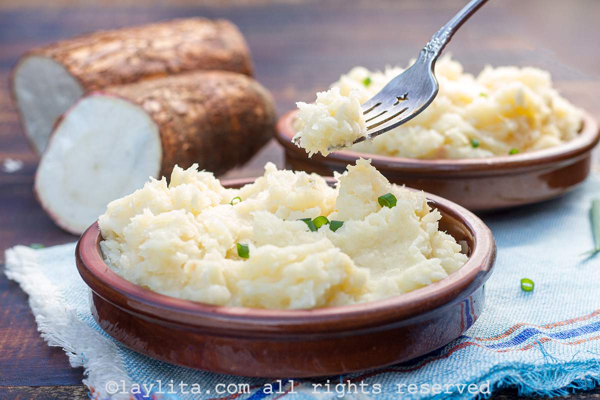Mashed yuca in a bowl with a hand holding a fork with a bite on it