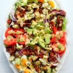 Overhead shot of a large white platter filled with chicken cobb salad on a white background