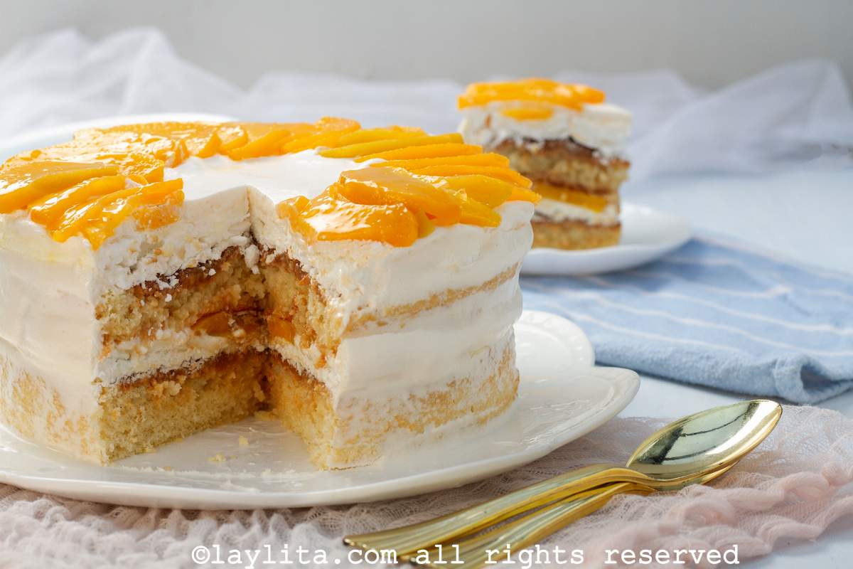 Side view of layered Uruguayan torta chajá on a white serving plate with one slice on a plate in the background.