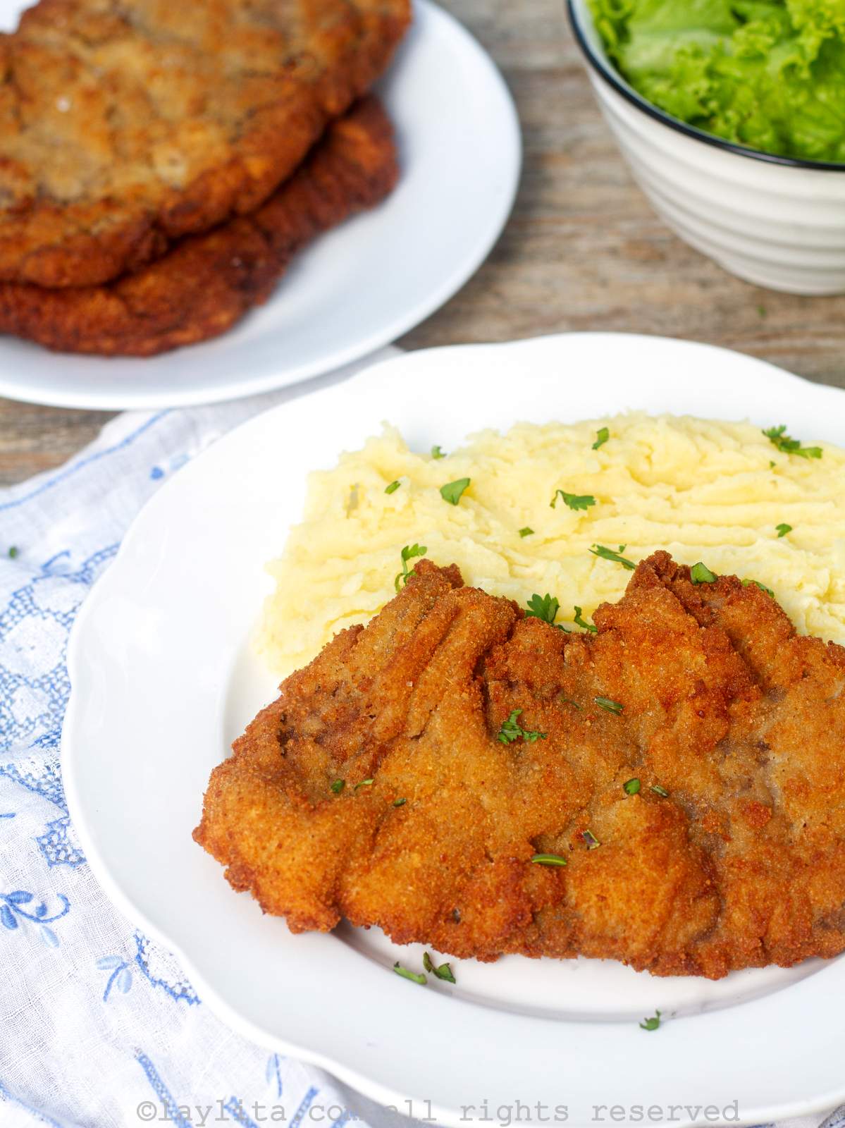 Overhead shot of milanesa breaded steaks with mashed potatoes next to a bowl of mashed potatoes. 