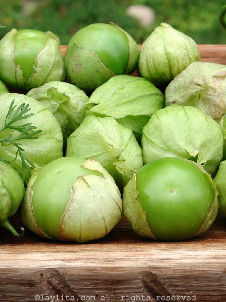 A wooden platter filled with green tomatillo fruits