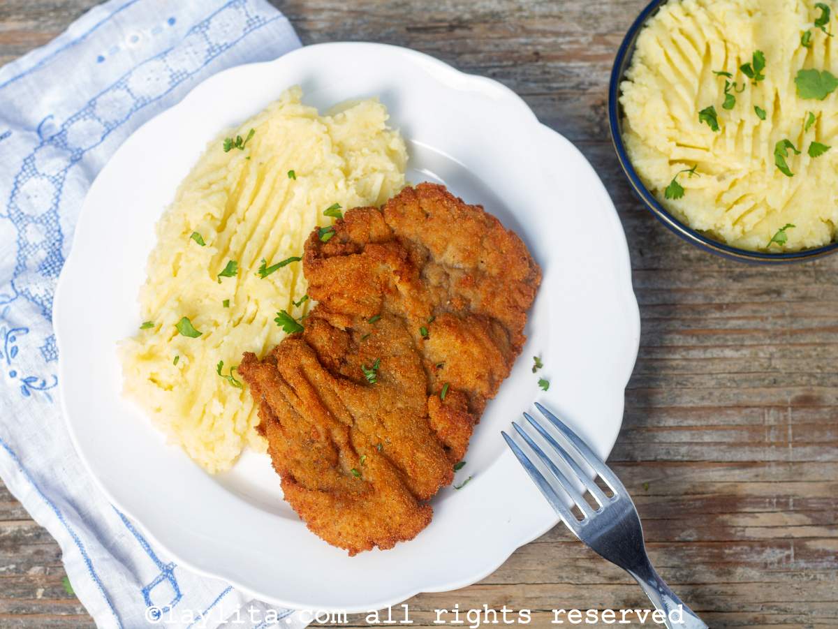 Overhead shot of crispy breaded steaks or milanesas de carne with mashed potatoes next to a bowl of mashed potatoes.