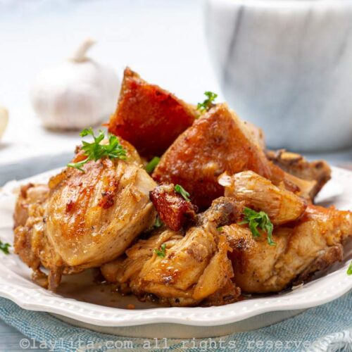 Pollo al ajillo on a white plate with whole roasted garlic cloves scattered throughout.