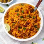 Overhead shot of arroz con gandules in a white bowl with lime wedges on the side and a bowl of olives in the background