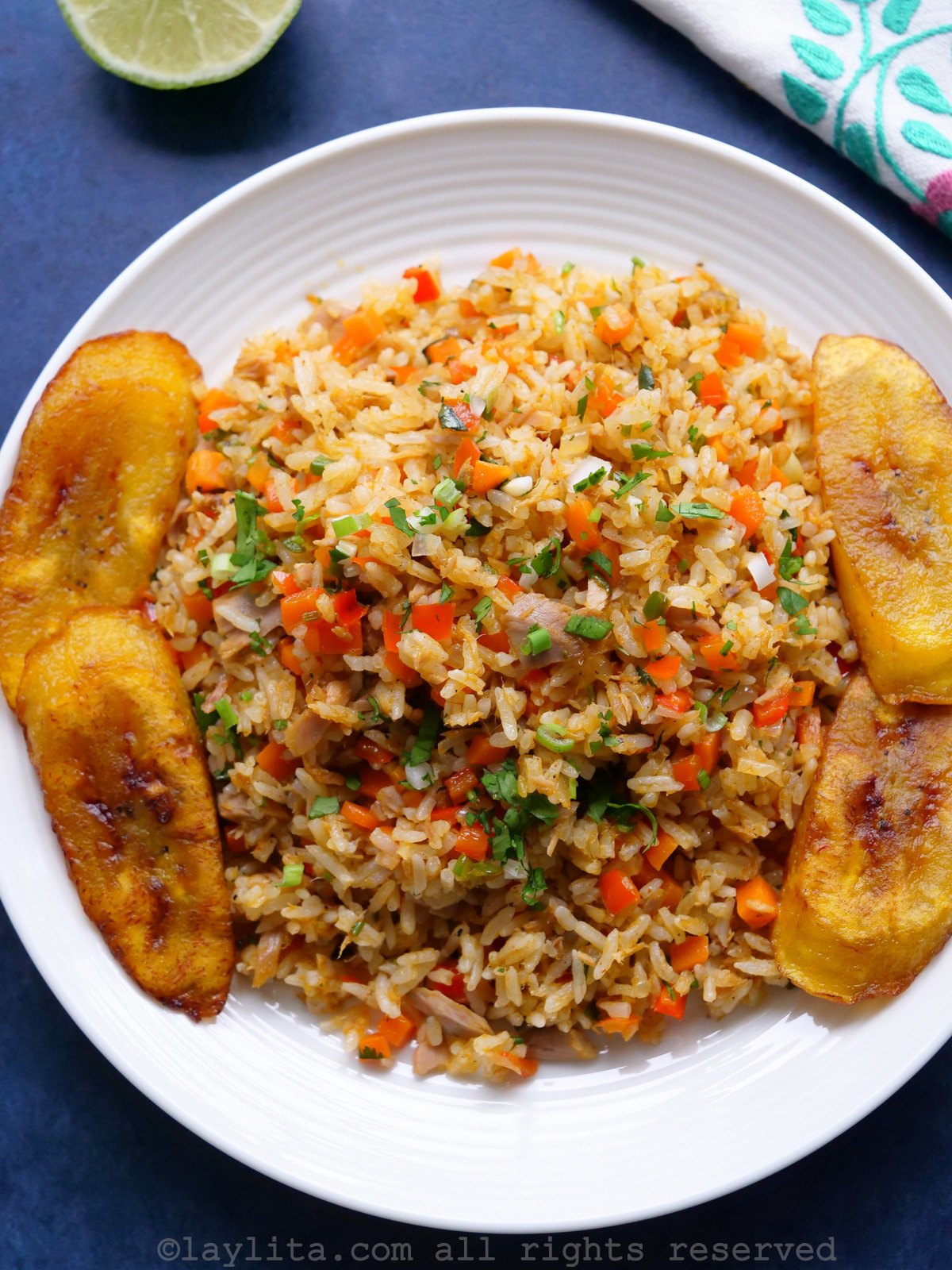 Overhead shot of rice with tuna fish and fried ripe plantains in a white plate on a blue background