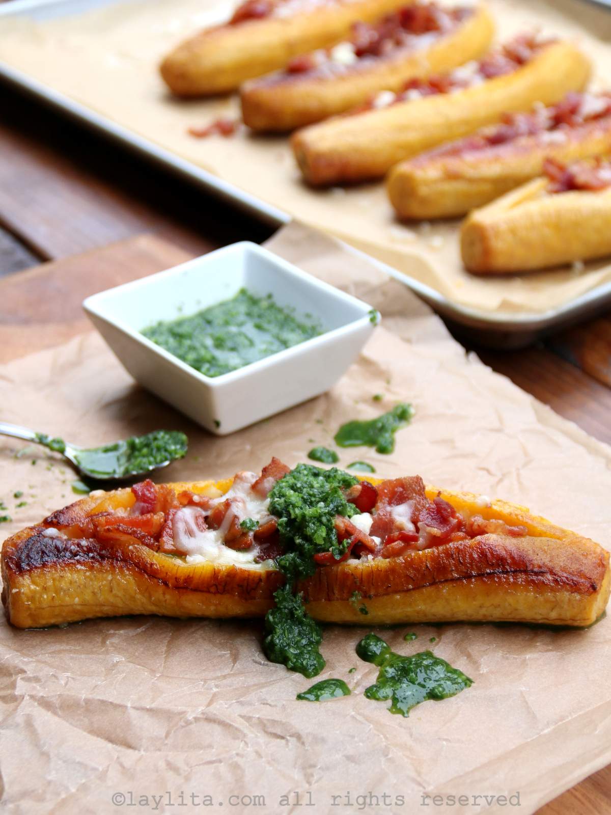 A ripe plantain baked and stuffed with cheese and bacon on a sheet of parchment paper, topped with spicy cilantro aji sauce