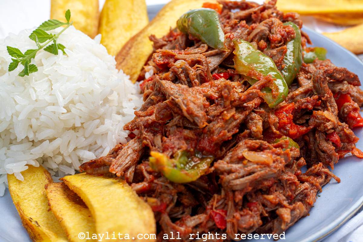 Close up of ropa vieja shredded beef stew with peppers served with rice and plantains on a plate.
