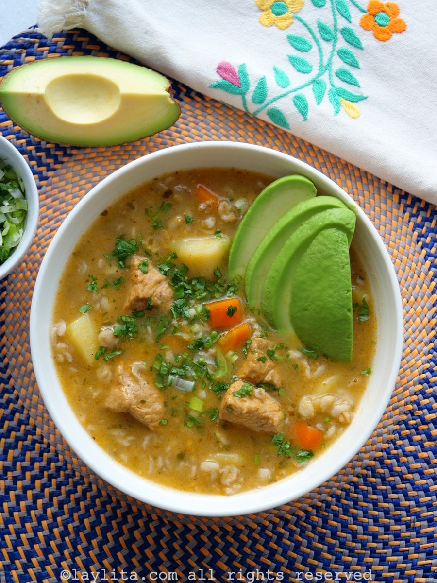 Bowl of Ecuadorian oat and pork soup with avocado slices on a round placement with a floral napkin