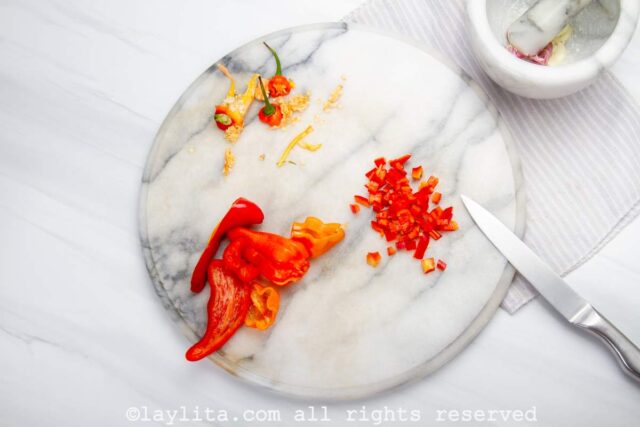 A white round board with red peppers being cut on it
