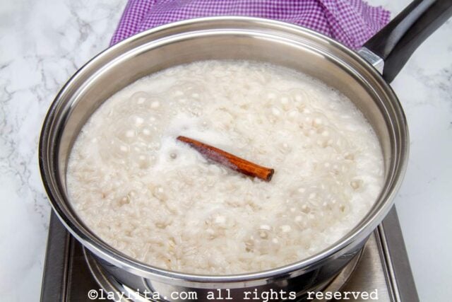 A pot of rice cooking with a cinnamon stick