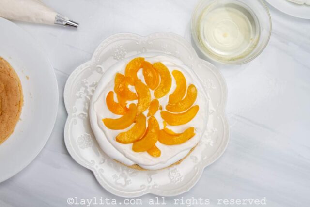 Adding a layer of whipped cream and sliced peaches on top of the meringue disc