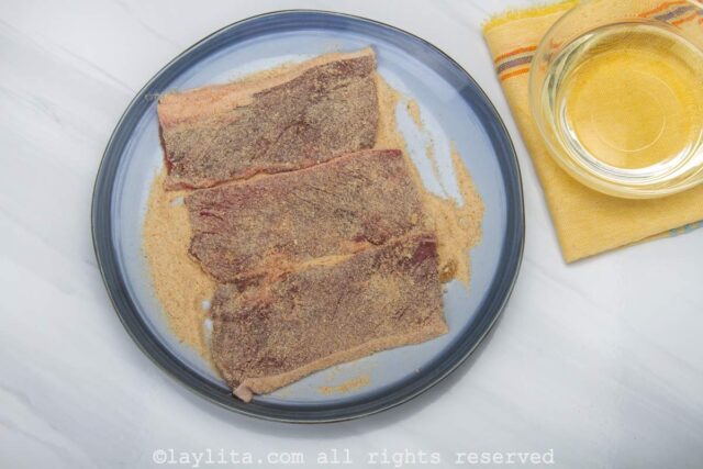 Thin steaks being coated in breadrumbs