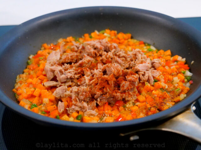 Canned tuna fish and red spice being added to a pan of diced vegetables