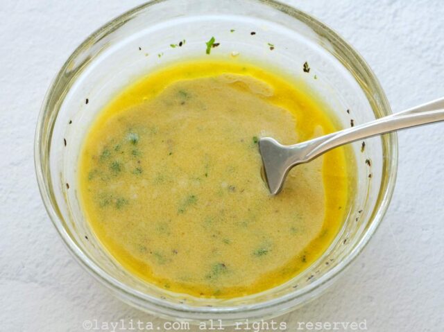 Red wine vinagar mustard dressing being mixed in a glass bowl on a white backgroun