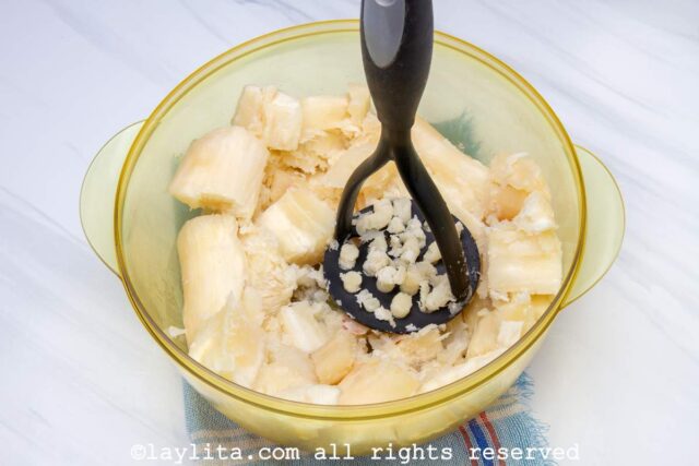 Cooked yuca or cassava pieces being mashed in a bowl