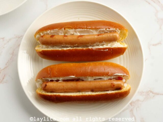 Two hot dog buns filled with sausages on a white plate
