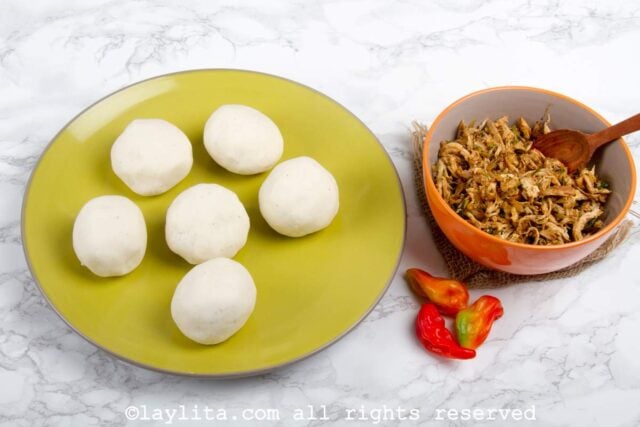 Balls of cornmeal empanada dough next to a bowl of chicken guiso filling