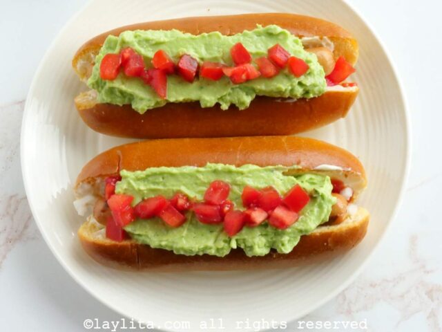 Two chilean completo hot dogs on a white plate with a white background