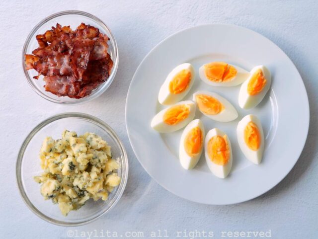 Quartered boiled eggs, bacon and crumbled cheese on three different plates