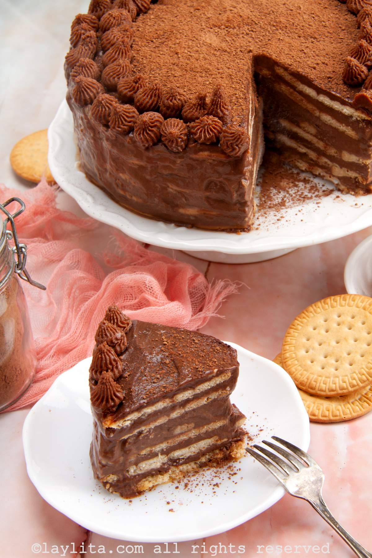 Slice of marquesa de chocolate on a plate with the rest of the cake on a cake stand.