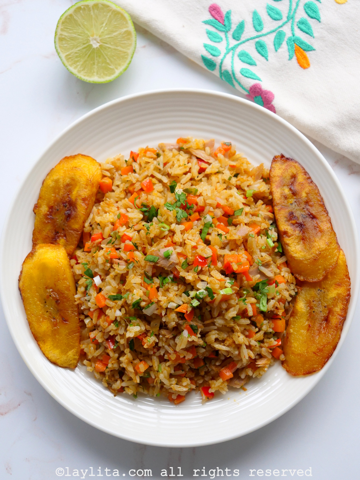 Overhead shot of tuna fish fried rice served on a white plate with plantains with green onions on top.