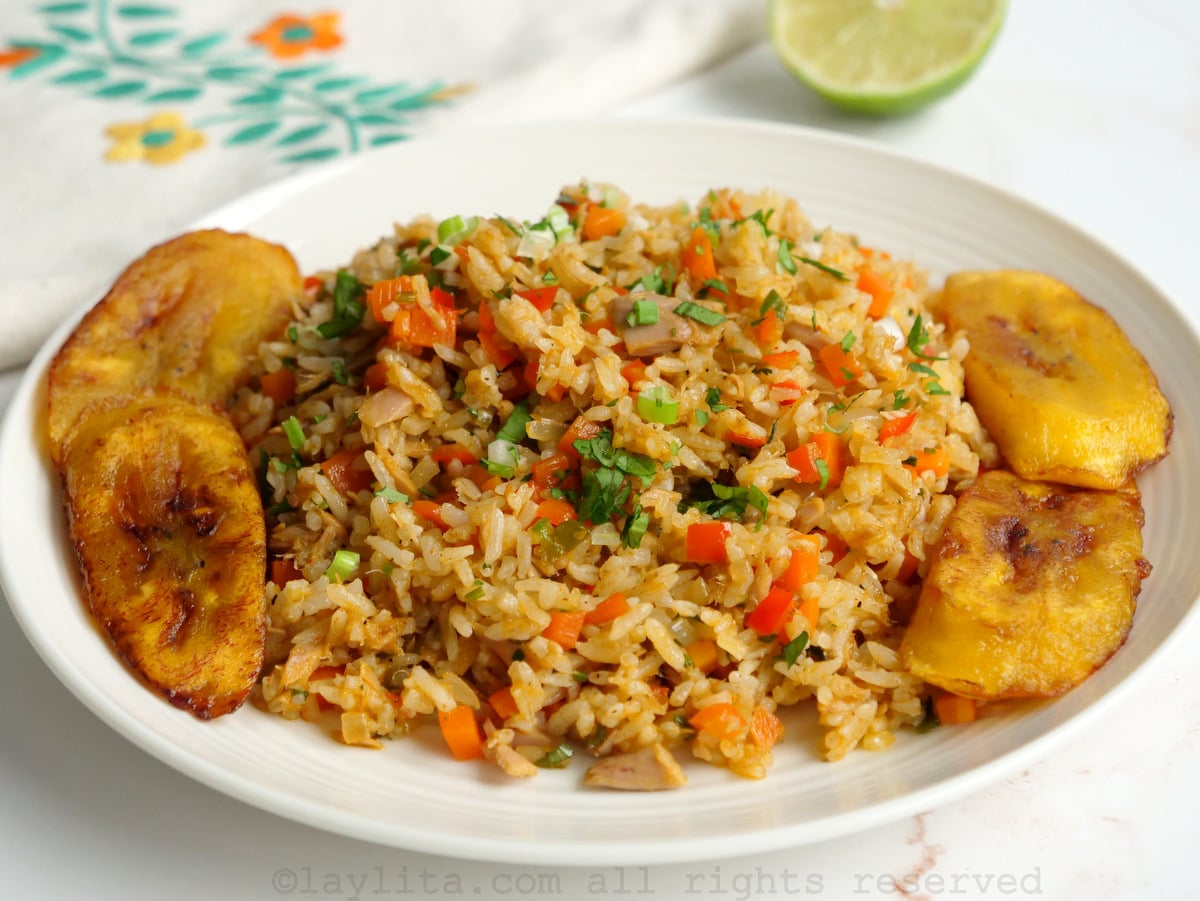 Side view of tuna fish fried rice served on a white plate with fried plantains on a white background.