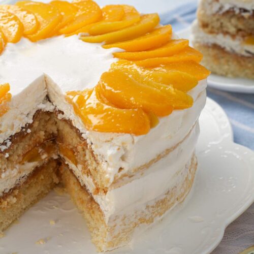 Close up of the Uruguayan torta chajá topped with sliced peaches with one slice missing to show the layers.