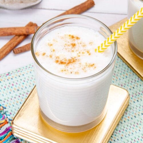 A glass of Venezuelan chicha topped with cinnamon served with a yellow straw.