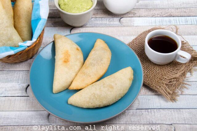Three cornmeal empanadas on a blue palte next to a cup of coffee