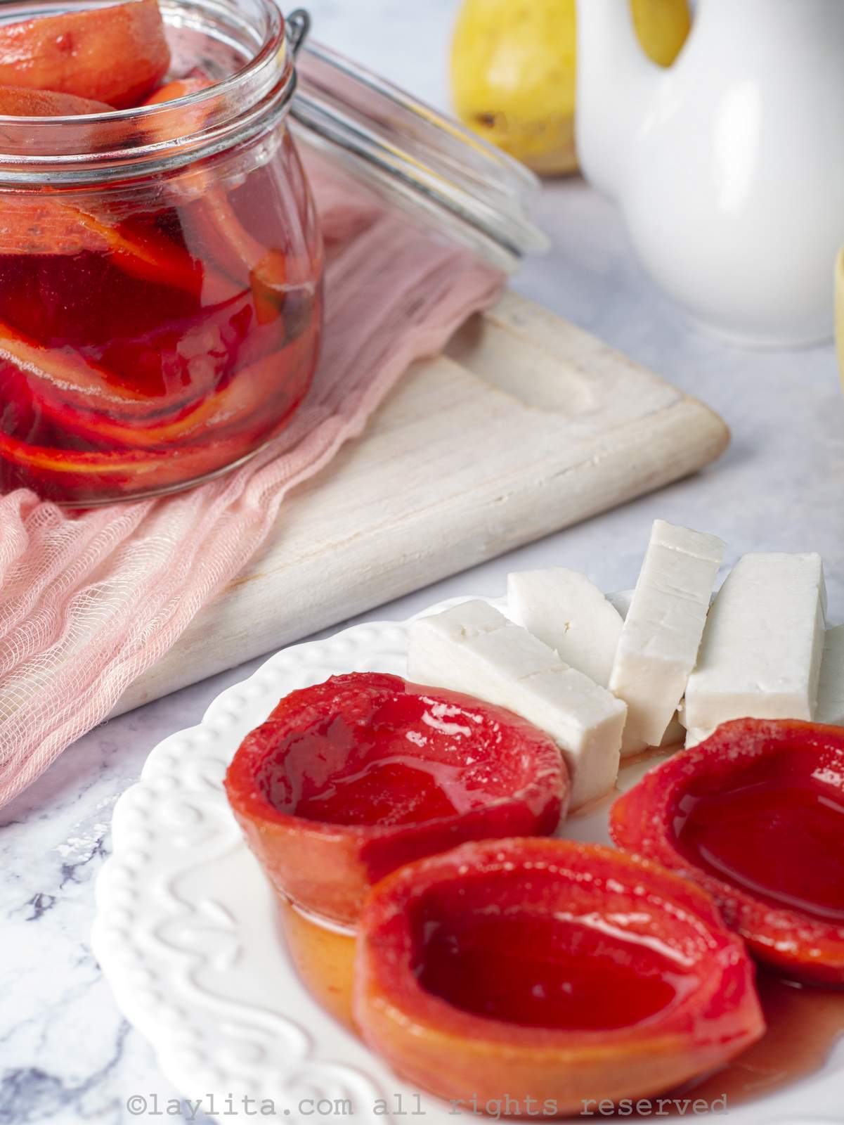 Closeup of cascos de guayaba or guava shells in syrup on a plate with cheese slices, with a jar of guava shells in the background