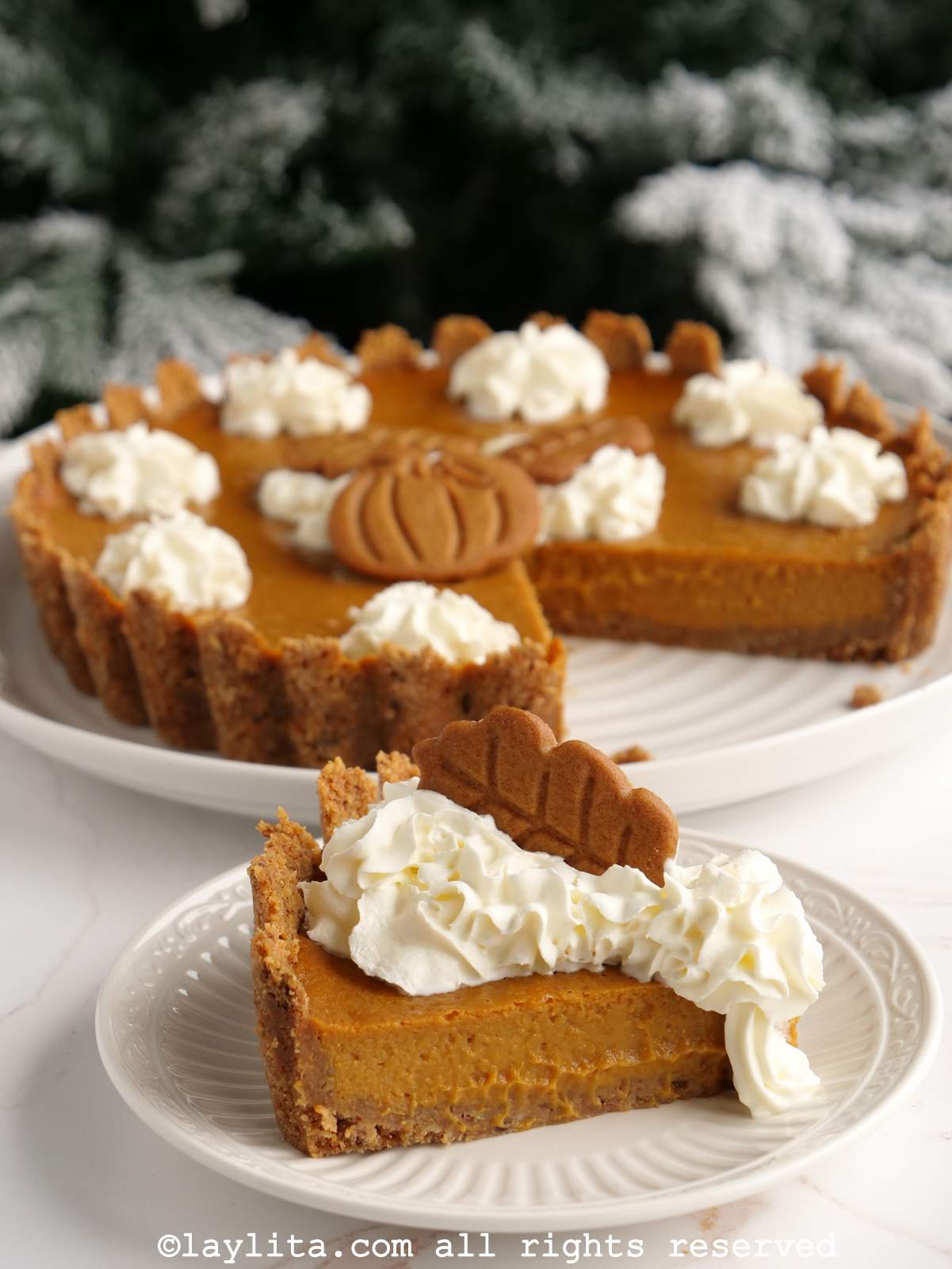 Slice of pumpkin pie with gingerbread cookies and whipped cream on top with the rest of the pie in the background.