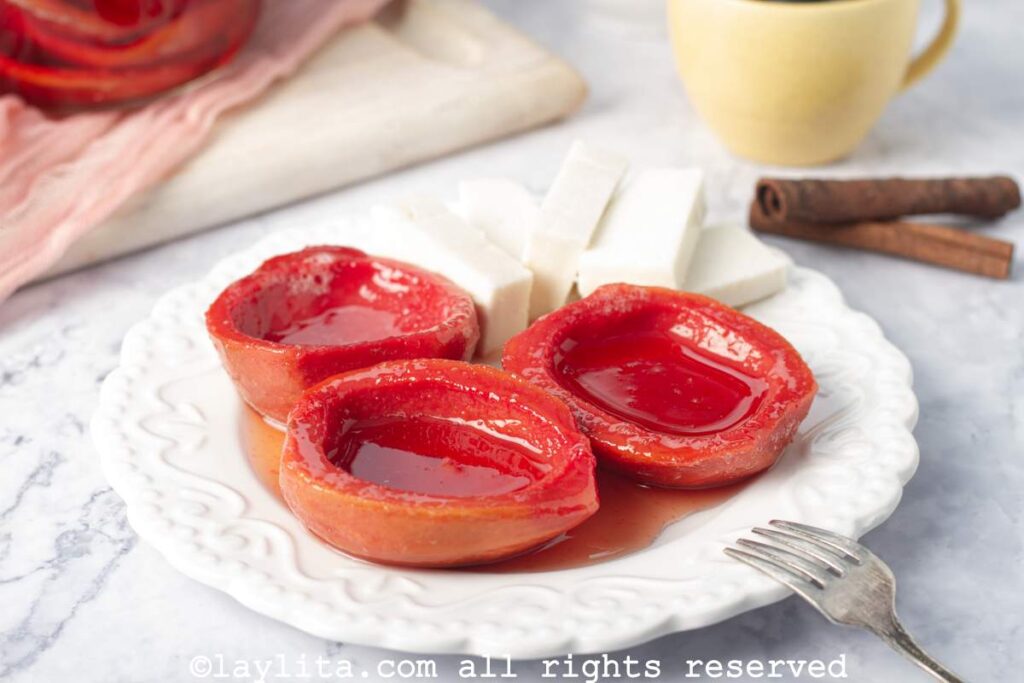 Three pink candied guava shells in syrup on a plate next to three slices of cheese