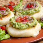 Close-up of tortilla de yuca or cheese stuffed cassava patties topped with avocado and tomato onion salsa